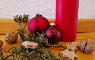 Stillleben mit Kerze, Weihnachtskugeln mit Karatedo-Schriftzeichen, Tannenzweigen, Keksen und Nüssen